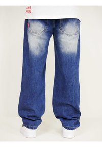 Baggy blue denim jeans with a faded wash, rear pockets, and elastic cuffs, paired with white sneakers.