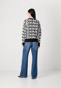 Juodas ir baltas megztinis su kartotiniais DKNY logotipų raštais, derinamas su aukštu liemeniu mėlynomis džinsomis ir juodais smailiais baletkais.