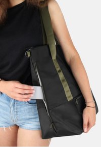 Schwarze Tragetasche mit olivgrünen Trägern, strukturiertem Stoff, einem Reißverschlussfach und einem Seitenfach für Karten oder Schlüssel. Besitzt eine strukturierte Form.