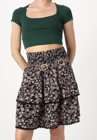 Green cropped top with a square neckline paired with a black floral tiered skirt featuring a gold circle belt and lace trim.