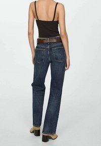 Jeans de tiro alto de color azul oscuro con un diseño de pierna recta, cinco bolsillos y un cinturón de cuero marrón. La tela muestra un acabado texturizado.