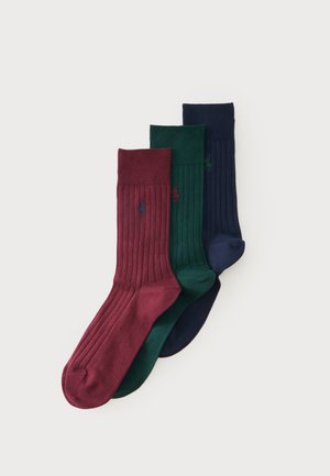 Trois chaussettes montantes côtelées en bordeaux, vert et marine, chacune avec un petit logo brodé sur le côté.