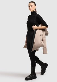 Black turtleneck sweater, fitted black leggings, and chunky black ankle boots. Holds a light beige puffer jacket with a black strap.