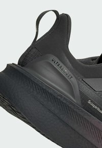 Černá sportovní bota s texturovaným svrškem, zesíleným podpatkem a silnou, vzorovanou podešví. Na boku je viditelné označení "ULTRABOOST".