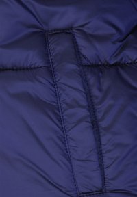 Materiał kurtki puchowej w kolorze granatowym o gładkiej, błyszczącej fakturze. Charakteryzuje się przeszywanymi panelami i ukrytym zamkiem błyskawicznym w kieszeni.