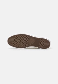 Semelle de chaussure en caoutchouc marron avec un motif de grip en forme de losange. Les bords sont blancs. Présente des lignes texturées et des détails de marque.