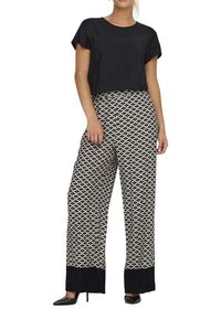 Un haut noir court associé à un pantalon large avec un motif géométrique en noir et blanc et des accents navy en bas. Des talons noirs.