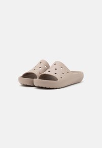Lysebeige slip-on sandaler lavet af formet gummi, med ventilationshuller, en tekstureret sål for greb og et minimalistisk design.