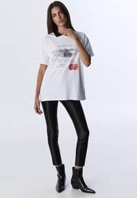 White short-sleeve T-shirt with graphic print, black collar, and red accents. Paired with shiny black fitted leggings and ankle boots.