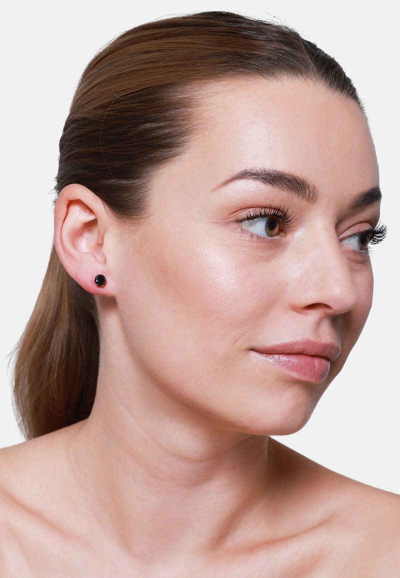 Boucles d'oreilles noires en forme de fleur, reposant sur un lobe d'oreille lisse, sur un fond blanc uni.