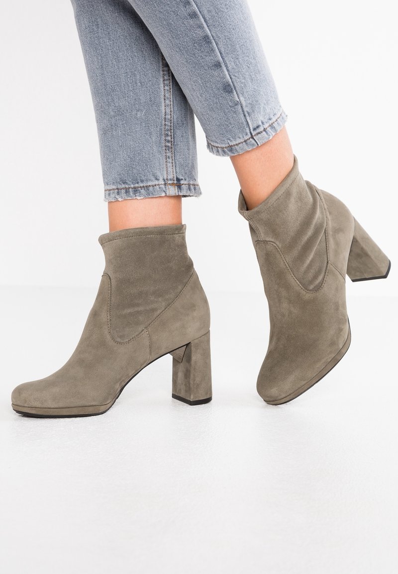 Femme portant des bottines en daim gris clair à talons blocs et un jean court bleu clair sur fond blanc.