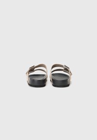 Brune sandaler med to justerbare stropper, en lav svart gummisåle og en glatt tekstur. Bakfra fremhever spenne-detaljen og det minimaliste designet.