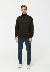 Sötétbarna garbós pulóver hosszú ujjal, kék nadrággal és fehér sportcipővel párosítva. Simaság és egyszerű design jellemzi.