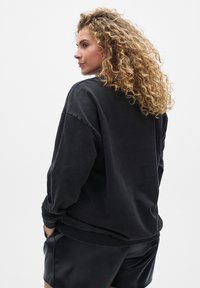 Čierny oversized sveter s okrúhlym výstrihom, voľným strihom a dlhými rukávmi, skombinovaný s čiernymi šortkami. Mäkkučká textília s minimálnou štruktúrou.