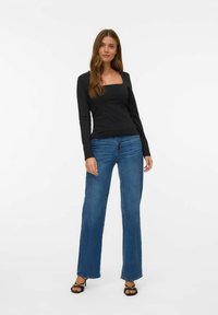 Zwarte top met lange mouwen en een vierkante halslijn, gecombineerd met lichtblauwe wijd-uitlopende jeans. De outfit heeft een casual ontwerp en zachte texturen.