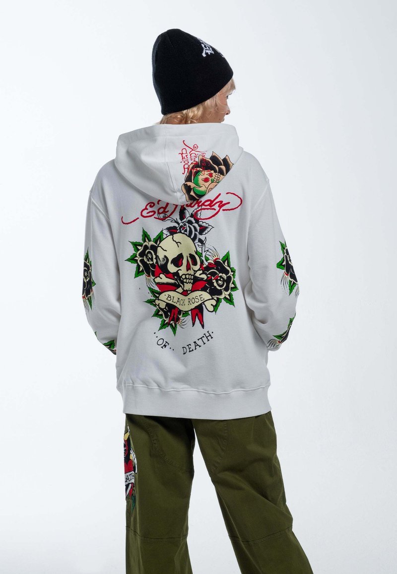 Sudadera blanca con un gráfico de calavera y rosa en la parte posterior, con acentos en verde y rojo. Mangas largas decoradas con diseños similares.