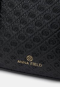 Czarna torebka o teksturowanym wykończeniu z wytłoczonym kwiatowym wzorem, złotym logo z napisem "ANNA FIELD" oraz z klasycznym kształtem.