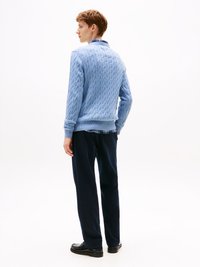 Pullover em azul claro, com ponto trançado e punhos e bainha canelados, combinado com calças azul-marinho e mocassins pretos, visto de costas.