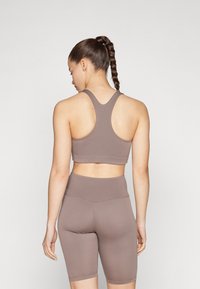 Brown sports bra with racerback design, paired with matching high-waisted bike shorts. Material is smooth, stretchy, and fitted.