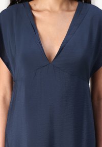 Rochie bleu marin cu decolteu în V și mâneci scurte. Confectionată dintr-un material texturat, prezintă o talie strânsă.