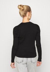 Černý pruhovaný svetr s přiléhavými dlouhými rukávy, kulatým výstřihem a nařasením na ramenech. Nosený s světle šedými džíny.