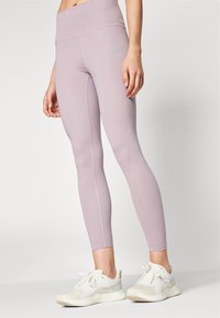 Lys lilla høyhalsede leggings med en glatt tekstur og flate sømmer, sammen med hvite treningssko med et gjennomsiktig mesh-design.