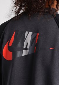 Svart sweatshirt med en stor röd och grå Nike-logotyp på baksidan, med en mjuk textur och design med rundad hals.