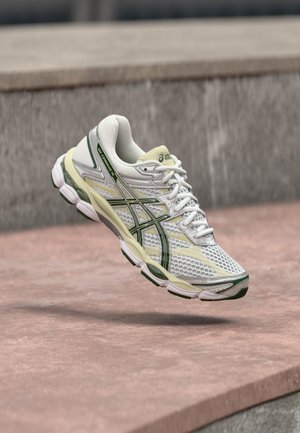 Chaussure de sport blanche avec une tige en maille, des accents verts et une semelle rembourrée. Dispose d'un design à lacets avec un col rembourré.