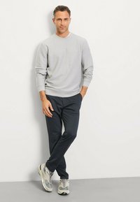 Helles graues Sweatshirt mit gerippten Bündchen und Saum, kombiniert mit dunklen Marineblauen Hosen und grauen Sneakers mit dezenten Akzenten.
