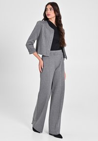 Completo grigio su misura con giacca corta e pantaloni a gamba larga. Tessuto testurizzato, top nero e silhouette slanciata e definita.
