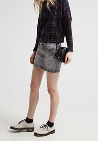 Šedá džínová mini sukně v kombinaci s námořnickou kostkovanou blůzou. Na nohou černé ponožky do kotníků a stříbrné oxfordky. Kabelka přes rameno v černé barvě.