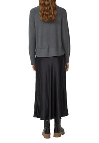 Pull gris avec bord côtelé, superposé sur une longue jupe en satin noir. La mannequin porte des bottes noires jusqu'au genou. Ses cheveux sont ondulés et long au niveau des épaules.