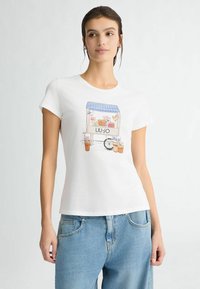 T-shirt en coton blanc avec un design coloré imprimé d'un chariot de fleurs avec des plantes en pot. Le t-shirt a un col rond classique et des manches courtes.