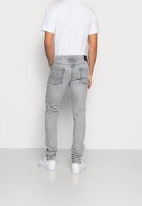 Grå denimjeans med slim fit, med fem fickor och en läderpatch på bakre midjan, i kombination med vita sneakers.