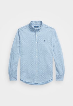 Lyseblå skjorte med knapper laget av vevd bomull, med geometrisk mønster, lange ermer og en liten brodert logo på brystet.