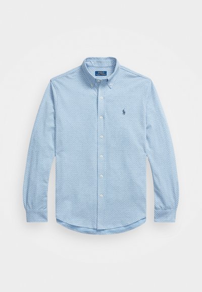 Gaiši zils pogājams krekls, izgatavots no audumam vītas kokvilnas, ar ģeometrisku rakstu, garām piedurknēm un mazu izšūtu logotipu uz krūtīm.