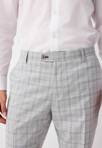 Pantaloni a quadri grigio chiaro realizzati in tessuto testurizzato, dotati di chiusura con un singolo bottone e dettagli delle tasche curati. Vestibilità sartoriale con accenti sottili.