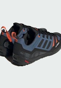 Niebieskie i czarne buty sportowe z pomarańczowymi akcentami, teksturowana tkanina, system sznurowania oraz wytrzymała podeszwa zaprojektowana do aktywności na świeżym powietrzu.