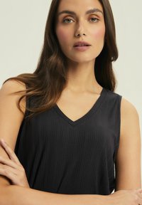 Black sleeveless top with a V-neck design, featuring vertical ribbed texture. Smooth fabric and relaxed fit, with a subtle sheen.