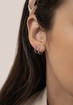 Silver hoop earrings adorned with small clear gemstones, featuring a curved shape and smooth finish, worn on a model's ear.