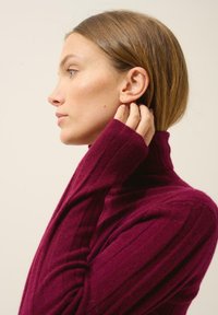 Jersey de cuello alto burdeos con textura acanalada, que cuenta con mangas alargadas, un diseño ajustado y un cuello alto, visto desde un perfil lateral.