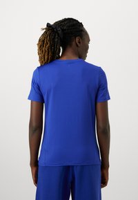 Zila sporta T-krekls ar īsām piedurknēm un apaļu kakla izgriezumu. Gluda tekstūra un viegls materiāls, ar mazu logotipu uz piedurknes.