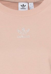 Ljust rosa Adidas t-shirt med ribbat mönster, som har en silverglittrande logotyp på bröstet och en standard rund halsringning.
