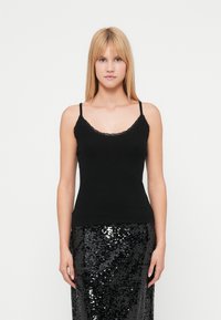 Μαύρο ριμπ τοπ με λεπτές τιράντες και ντεκολτέ με δαντέλα σε κυματιστό σχέδιο, συνδυασμένο με μαύρη φούστα με παγιέτες. Απλό και εφαρμοστό σχέδιο.