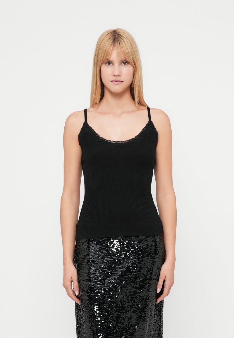 Μαύρο ριμπ τοπ με λεπτές τιράντες και ντεκολτέ με δαντέλα σε κυματιστό σχέδιο, συνδυασμένο με μαύρη φούστα με παγιέτες. Απλό και εφαρμοστό σχέδιο.