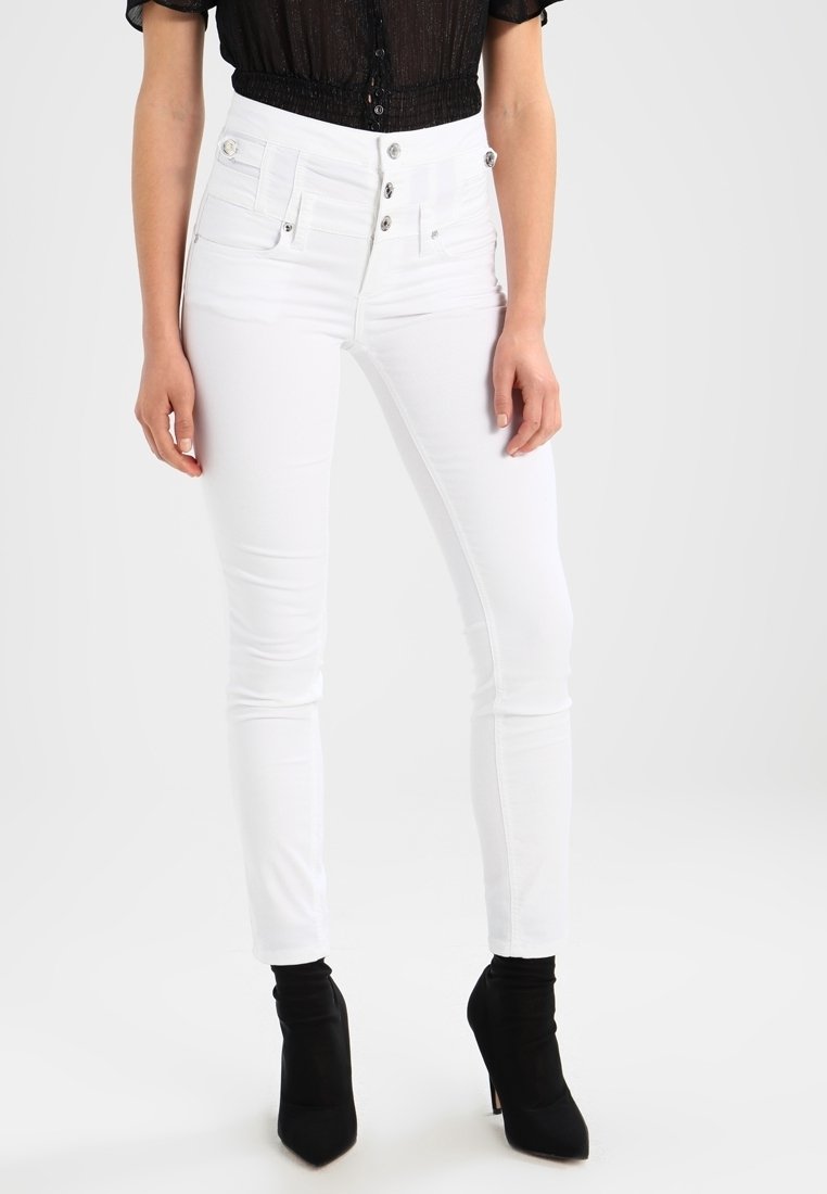Jeans ajustados blancos de cintura alta con cierre de cinco botones, bolsillos frontales y una tela suave y elástica. Combinados con botas negras hasta el tobillo.