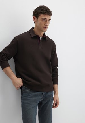 Dunkelbrauner Pullover mit Kragen und gerippten Bündchen. Verfügt über eine versteckte Knopfleiste, die mit einem weinroten Hemd darunter kombiniert ist. Getragen mit blauen Jeans.