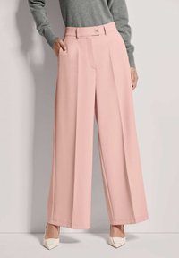 Lichtroze wijde broek met een zachte textuur, voorzien van een voorplooien en dubbele knoopsluiting in de taille. Gecombineerd met witte hakken.