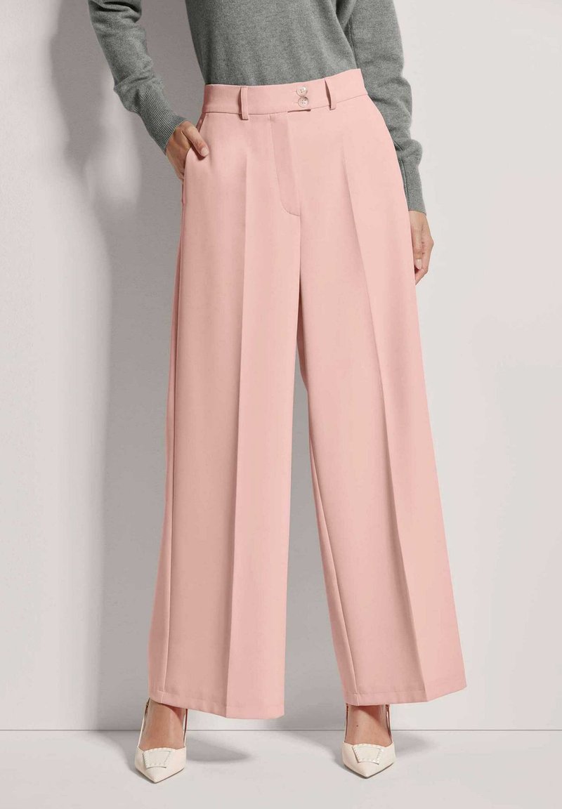 Lichtroze wijde broek met een zachte textuur, voorzien van een voorplooien en dubbele knoopsluiting in de taille. Gecombineerd met witte hakken.