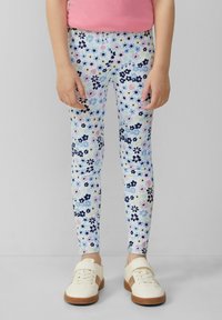 Leggings mit einem mehrfarbigen Blumenmuster auf einem hellen Hintergrund, einem elastischen Bund und einer schlanken Passform. Kombiniert mit weißen Sneakers.